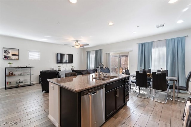 kitchen featuring visible vents, stone counters, a kitchen island with sink, a sink, and dishwasher