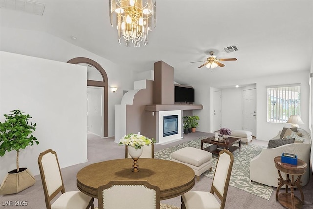 dining space featuring carpet flooring, ceiling fan with notable chandelier, visible vents, and a glass covered fireplace