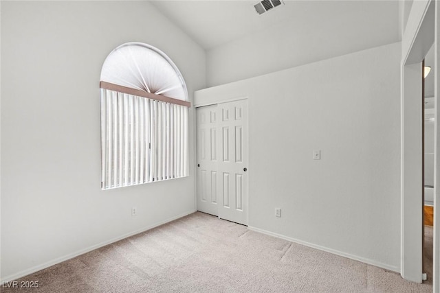 unfurnished bedroom with visible vents, lofted ceiling, a closet, carpet floors, and baseboards