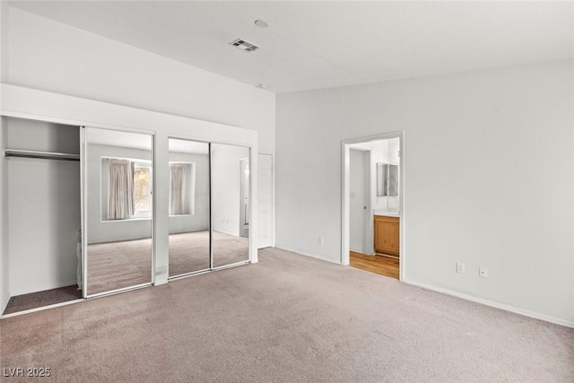 unfurnished bedroom with carpet flooring, visible vents, two closets, and connected bathroom