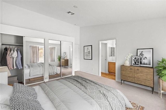 carpeted bedroom featuring ensuite bath, vaulted ceiling, visible vents, and multiple closets