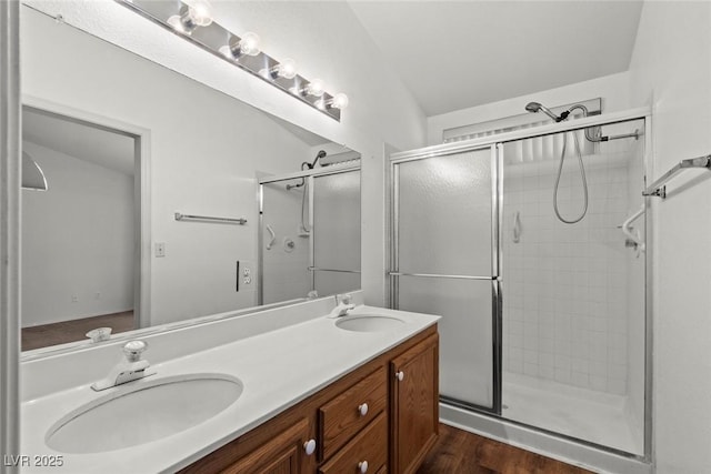 bathroom featuring double vanity, a shower stall, wood finished floors, and a sink