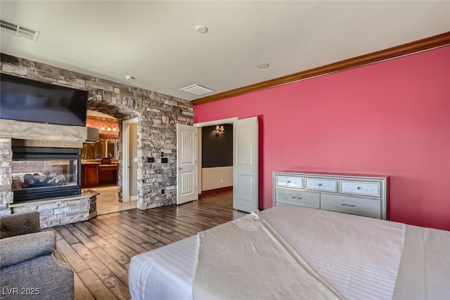 bedroom featuring a stone fireplace, crown molding, visible vents, and wood-type flooring