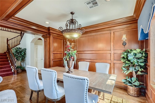 dining space with visible vents, crown molding, stairs, wood finished floors, and arched walkways