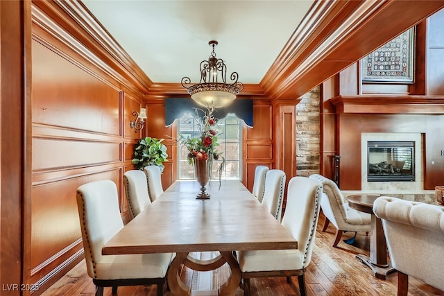 dining room with a notable chandelier, ornamental molding, a glass covered fireplace, hardwood / wood-style floors, and a decorative wall