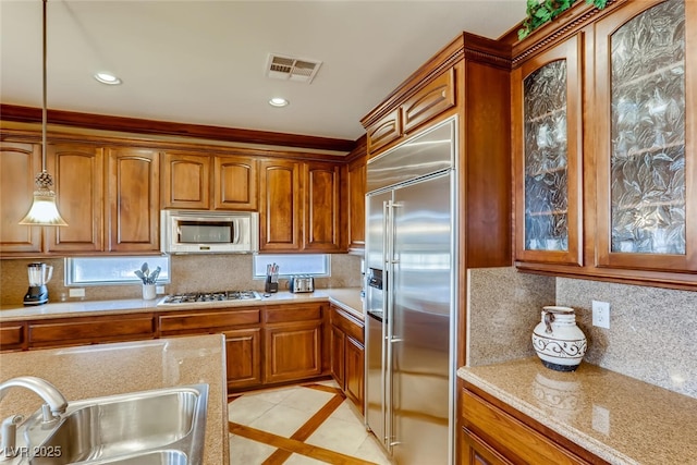 kitchen with brown cabinetry, visible vents, a sink, hanging light fixtures, and appliances with stainless steel finishes