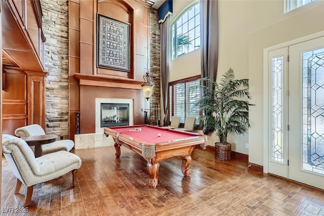 game room with a large fireplace, baseboards, a high ceiling, wood finished floors, and billiards