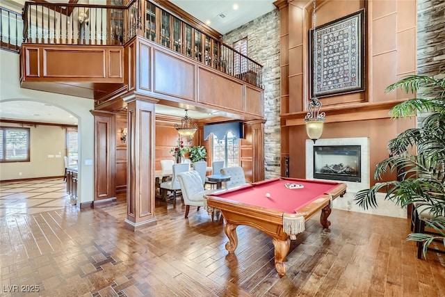 playroom with baseboards, ornate columns, a high ceiling, arched walkways, and a glass covered fireplace