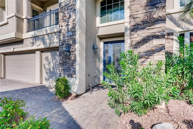 view of exterior entry with stone siding, stucco siding, an attached garage, and decorative driveway