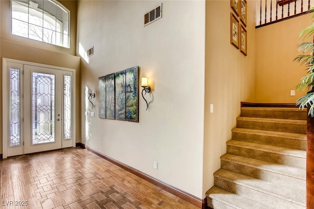 entryway with visible vents, baseboards, parquet flooring, stairway, and a towering ceiling