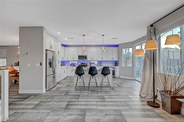 kitchen featuring a kitchen island, a breakfast bar, light countertops, appliances with stainless steel finishes, and white cabinets