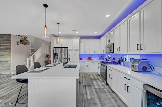 kitchen with a sink, stainless steel appliances, wine cooler, light wood-style floors, and a kitchen breakfast bar