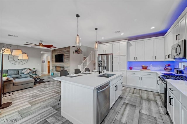 kitchen with a ceiling fan, a sink, open floor plan, stainless steel appliances, and light countertops