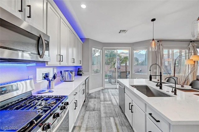 kitchen featuring visible vents, a sink, appliances with stainless steel finishes, white cabinetry, and decorative light fixtures