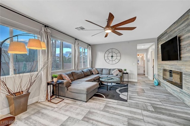 living area with a tiled fireplace, visible vents, baseboards, and ceiling fan