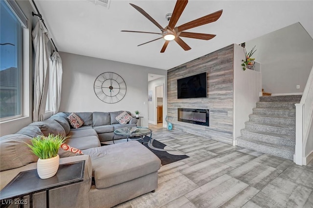 living area featuring wood finished floors, a fireplace, baseboards, ceiling fan, and stairs