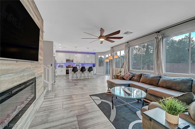 living area featuring a premium fireplace, visible vents, and ceiling fan