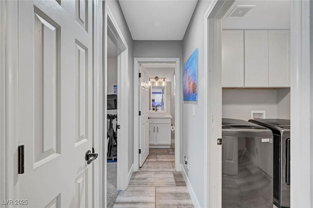 hall with washer and dryer, visible vents, baseboards, and light wood-style flooring