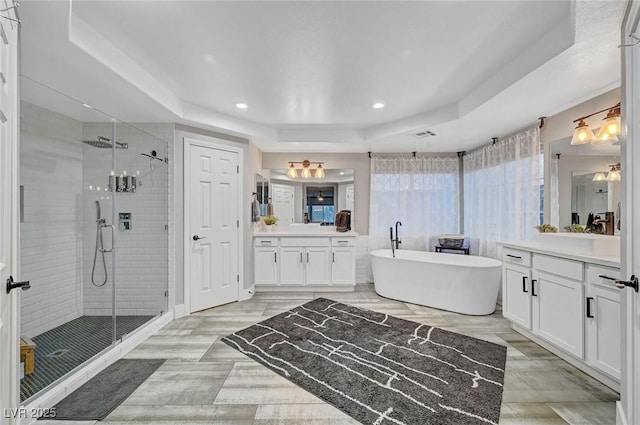 bathroom featuring a tray ceiling, recessed lighting, a shower stall, a soaking tub, and vanity