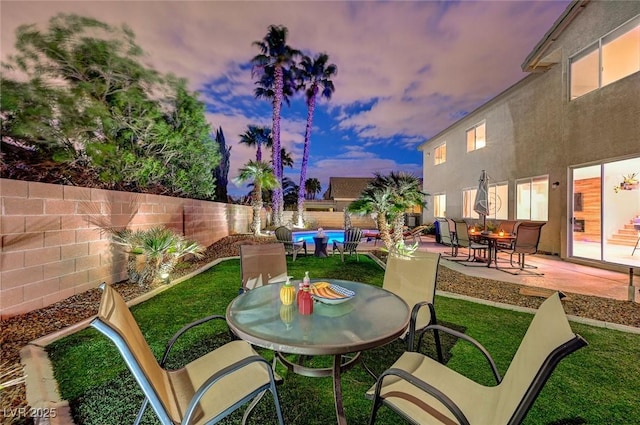 patio terrace at dusk featuring a yard, a fenced in pool, a fenced backyard, and outdoor dining space