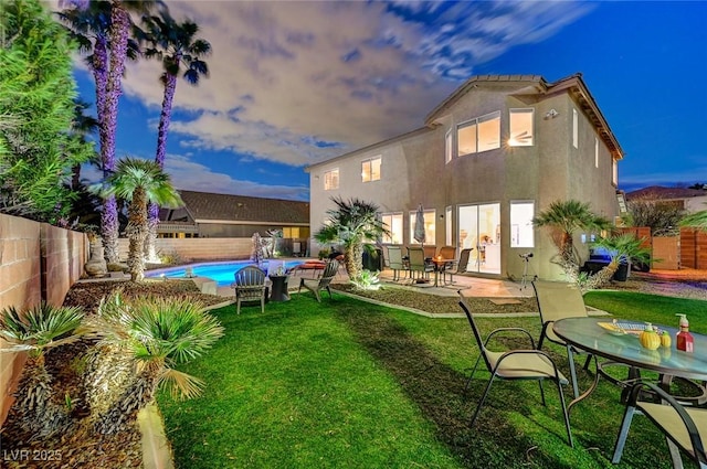 rear view of house featuring a fenced in pool, stucco siding, a lawn, a fenced backyard, and a patio