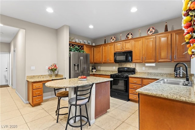 kitchen with a sink, black appliances, light tile patterned flooring, and brown cabinetry