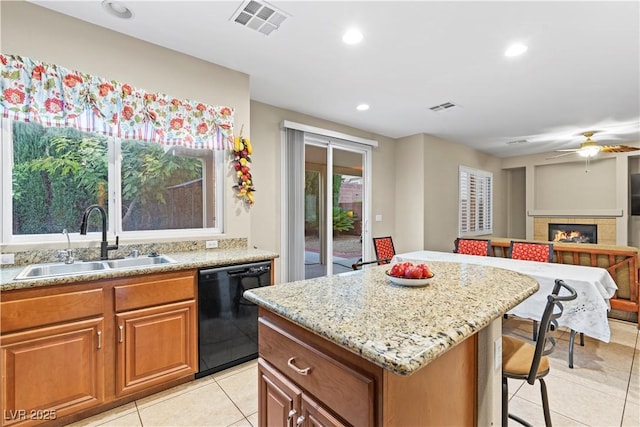 kitchen with light stone counters, visible vents, a sink, black dishwasher, and a tiled fireplace