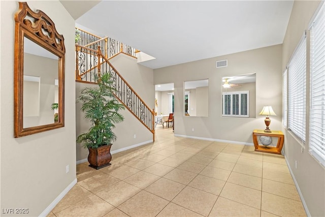 tiled foyer with stairway, visible vents, baseboards, and ceiling fan