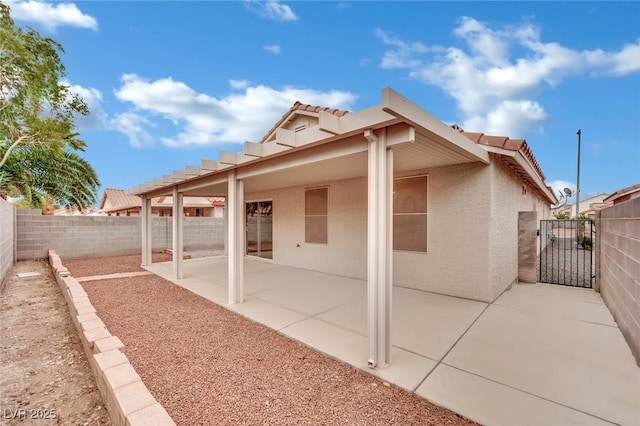 rear view of house featuring a tile roof, stucco siding, a fenced backyard, a patio, and a gate