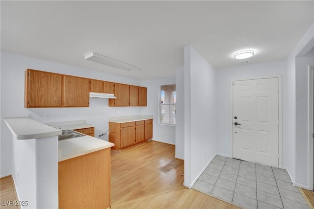 kitchen featuring brown cabinetry, a peninsula, light countertops, light wood-style floors, and under cabinet range hood