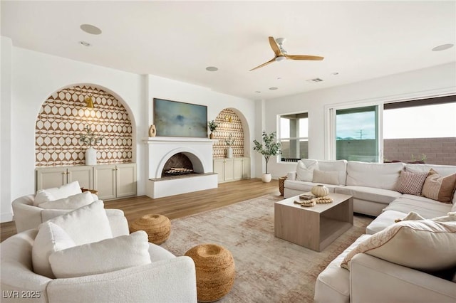 living room with a ceiling fan, visible vents, light wood-style flooring, recessed lighting, and a fireplace with raised hearth