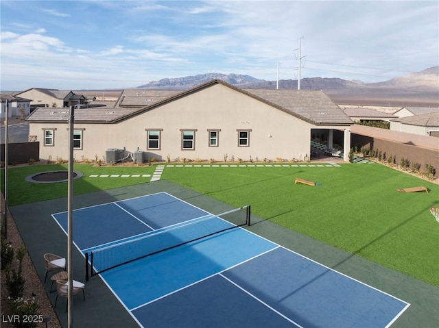 back of house featuring stucco siding, a lawn, a tennis court, fence, and a mountain view