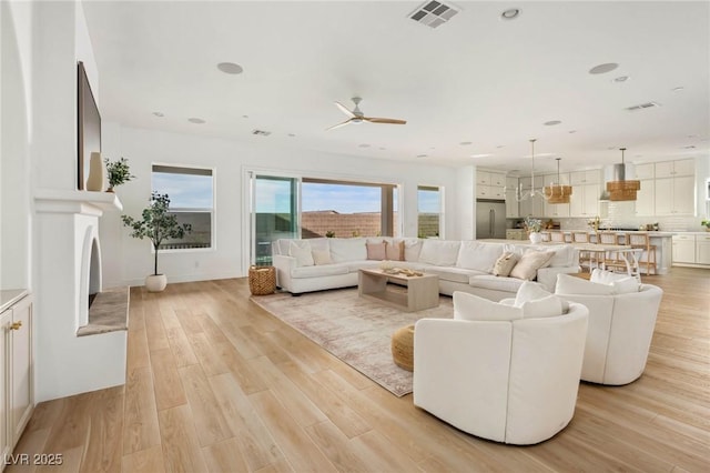 living area featuring a ceiling fan, light wood-style floors, and visible vents