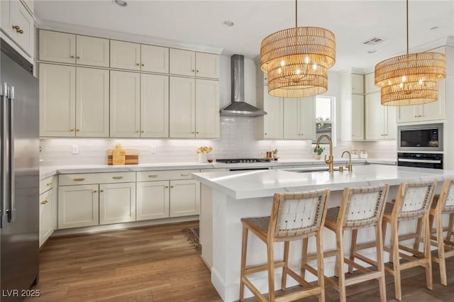 kitchen with visible vents, wall chimney range hood, appliances with stainless steel finishes, an inviting chandelier, and a sink