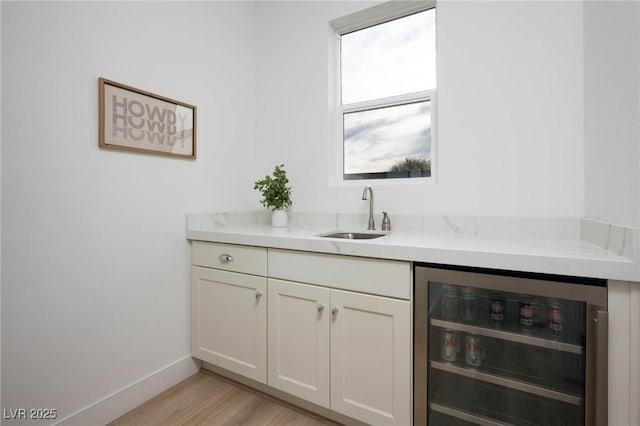 bar featuring beverage cooler, light wood-type flooring, baseboards, and a sink