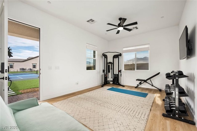 workout area featuring light wood-style floors, a ceiling fan, visible vents, and baseboards