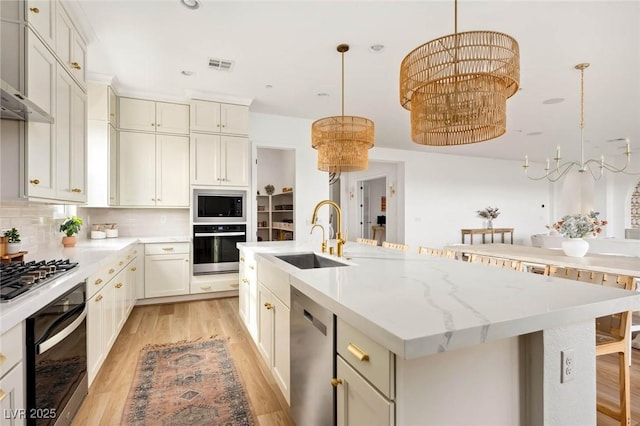 kitchen featuring a center island with sink, a sink, tasteful backsplash, appliances with stainless steel finishes, and wall chimney exhaust hood