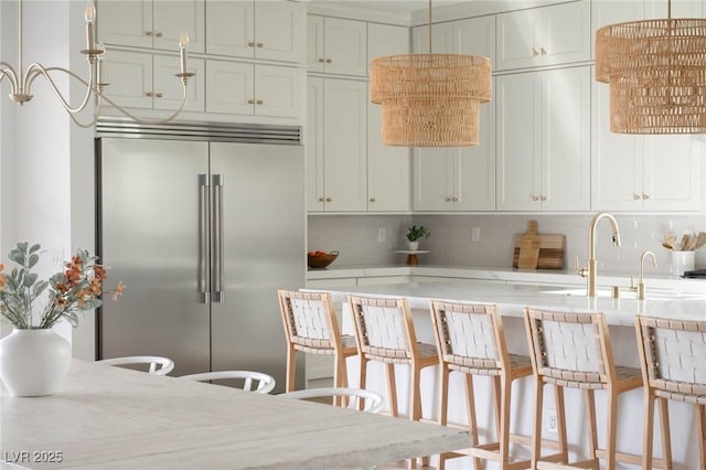 kitchen with tasteful backsplash, decorative light fixtures, built in refrigerator, light countertops, and a sink