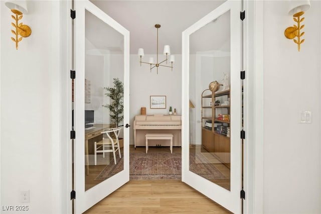 corridor with light wood-type flooring and an inviting chandelier