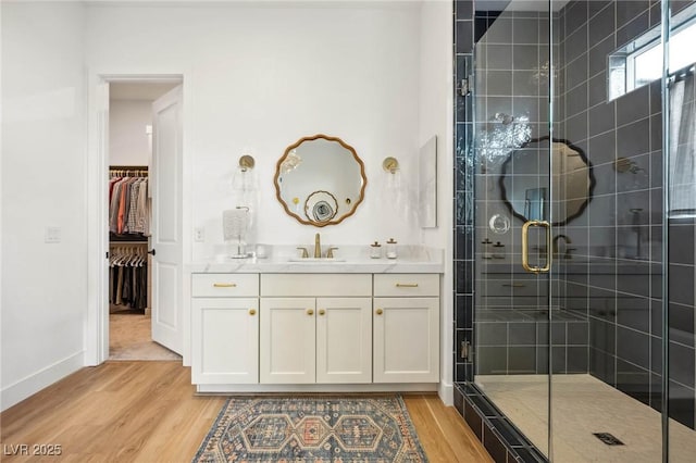 bathroom featuring a walk in closet, baseboards, wood finished floors, and a shower stall