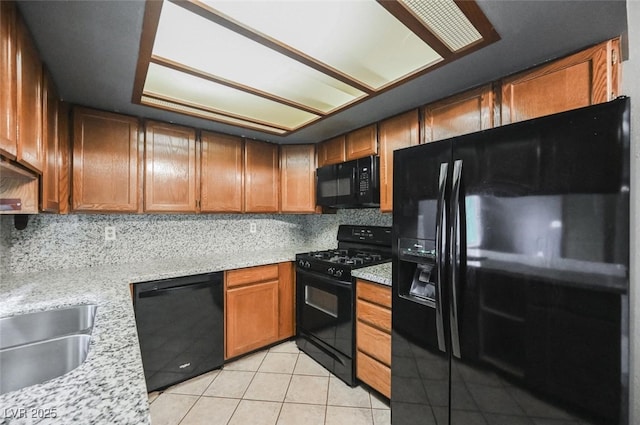 kitchen with brown cabinets, black appliances, a sink, backsplash, and light tile patterned floors