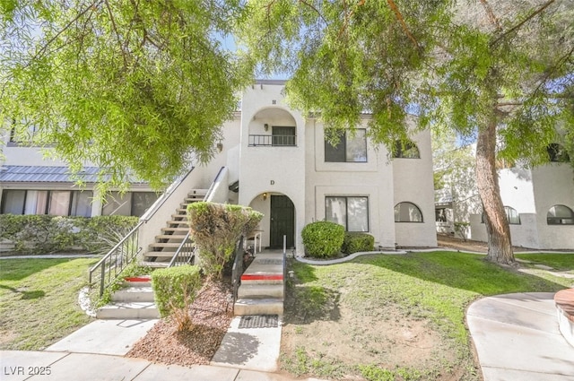 view of front facade featuring stairway, stucco siding, and a front yard