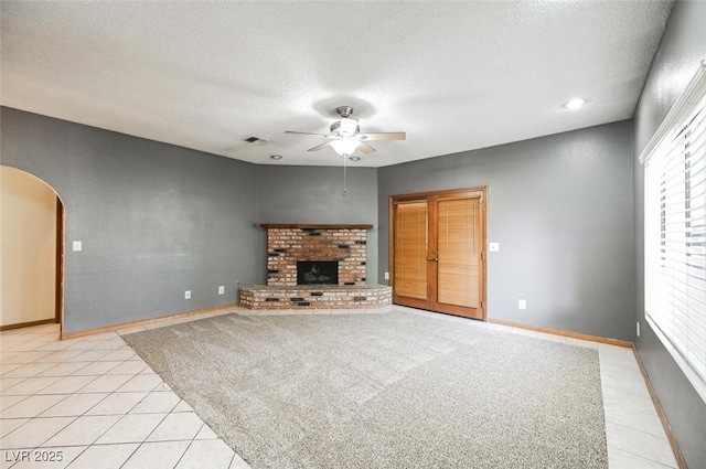 unfurnished living room featuring a ceiling fan, visible vents, arched walkways, a textured ceiling, and a brick fireplace