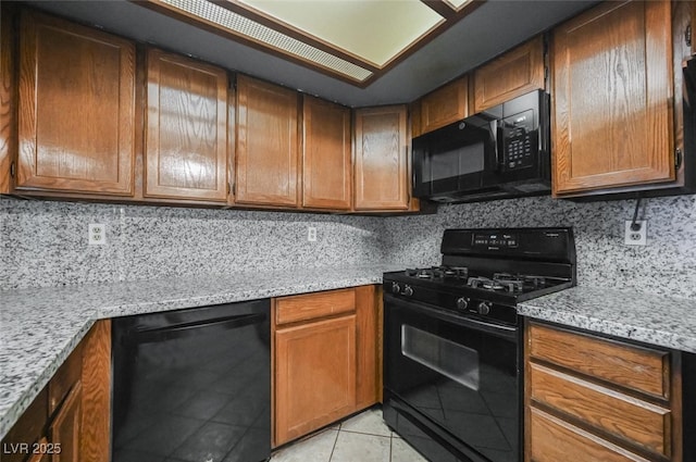 kitchen featuring light stone countertops, light tile patterned floors, decorative backsplash, brown cabinets, and black appliances