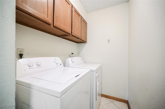 laundry room featuring washer and dryer, a textured ceiling, cabinet space, light tile patterned floors, and baseboards