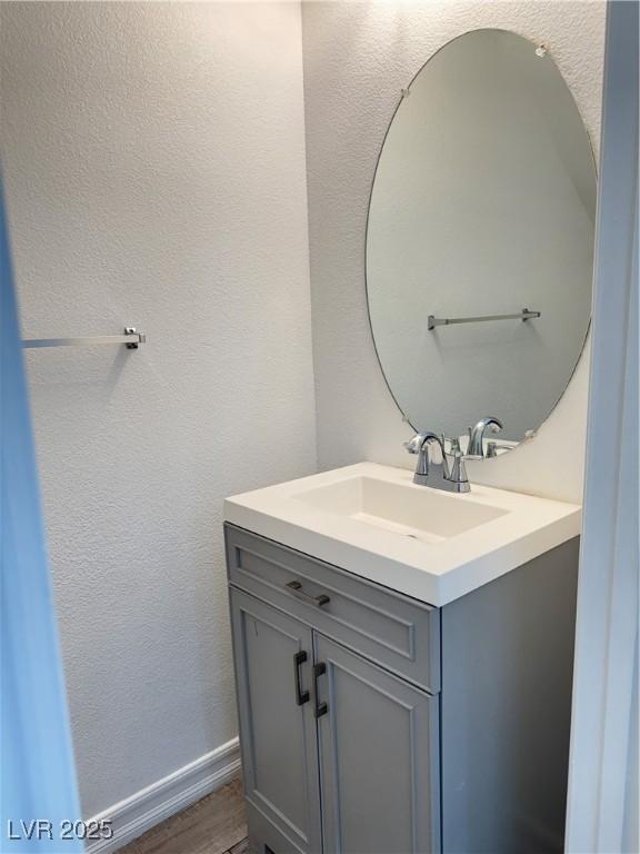 bathroom with vanity, wood finished floors, baseboards, and a textured wall