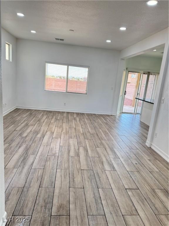 empty room featuring visible vents, plenty of natural light, a textured ceiling, and wood finished floors