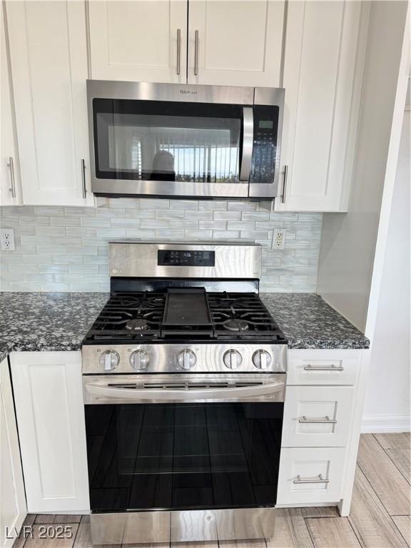 kitchen with wood tiled floor, decorative backsplash, dark stone countertops, appliances with stainless steel finishes, and white cabinetry