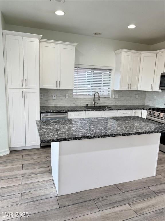 kitchen featuring a center island, dark stone counters, white cabinets, stainless steel appliances, and a sink