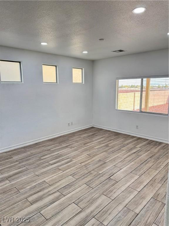 unfurnished room featuring light wood-style flooring, baseboards, visible vents, and a textured ceiling